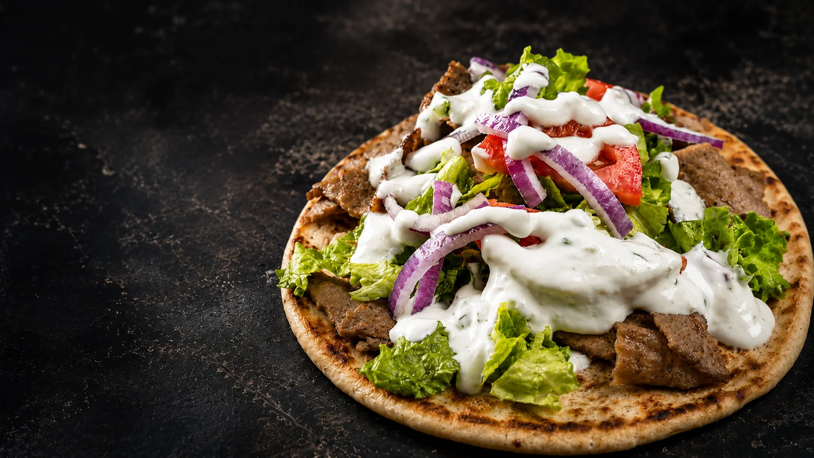 A loaded Gyro Rice and Spice gyro topped with ziki sauce, lettuce, tomato, and red onion on warm pita