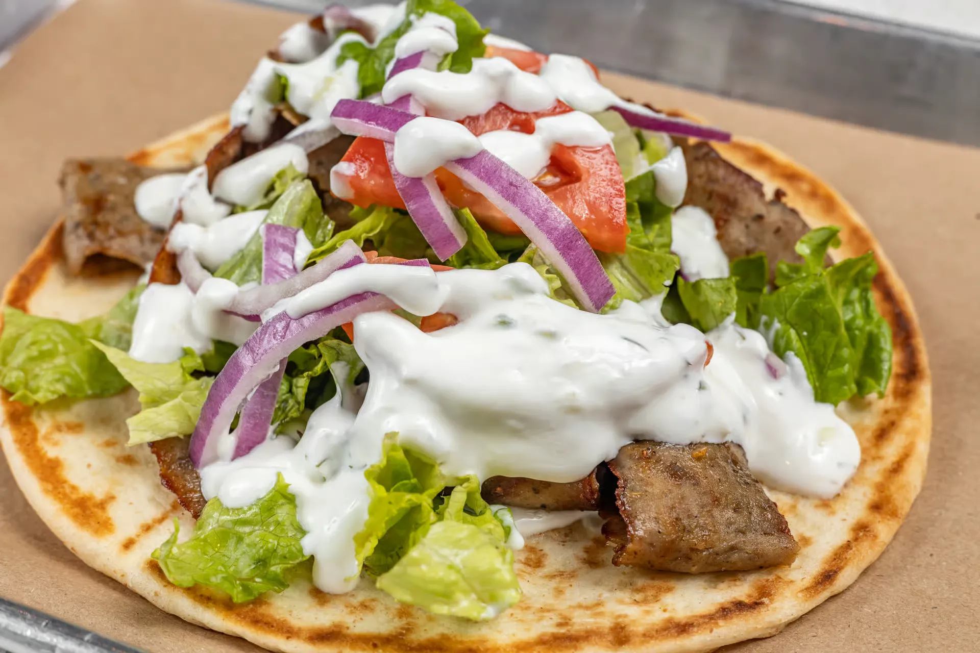 A loaded Gyro Rice and Spice gyro topped with ziki sauce, lettuce, tomato, and red onion on warm pita